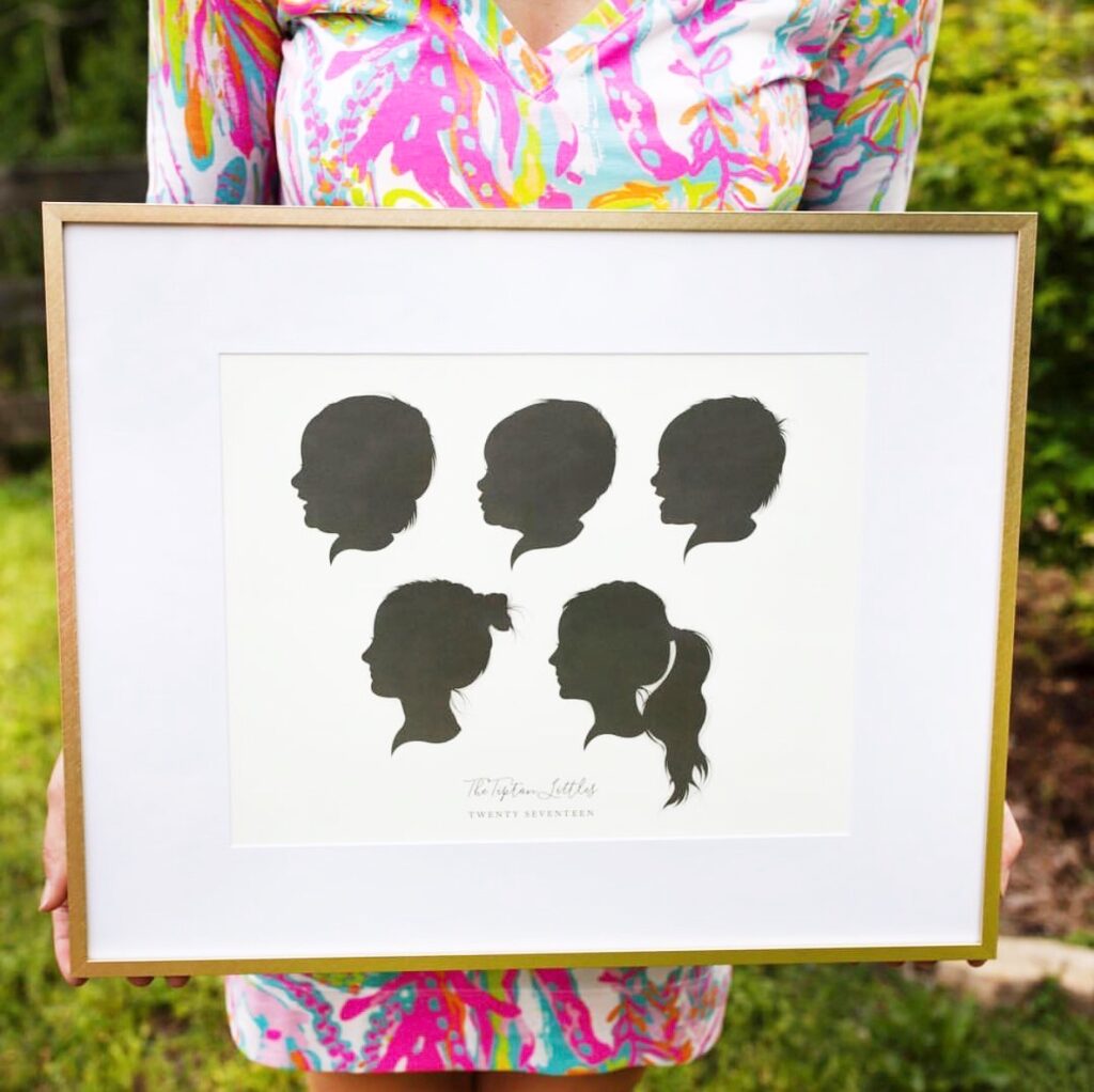 women holding frame of silhouettes of kids profiles.